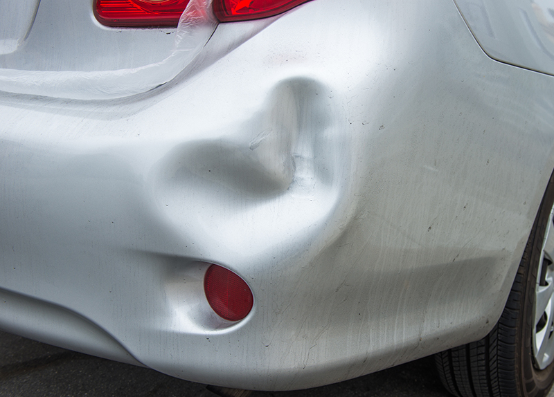 The bumper of a silver car, with a dent in it