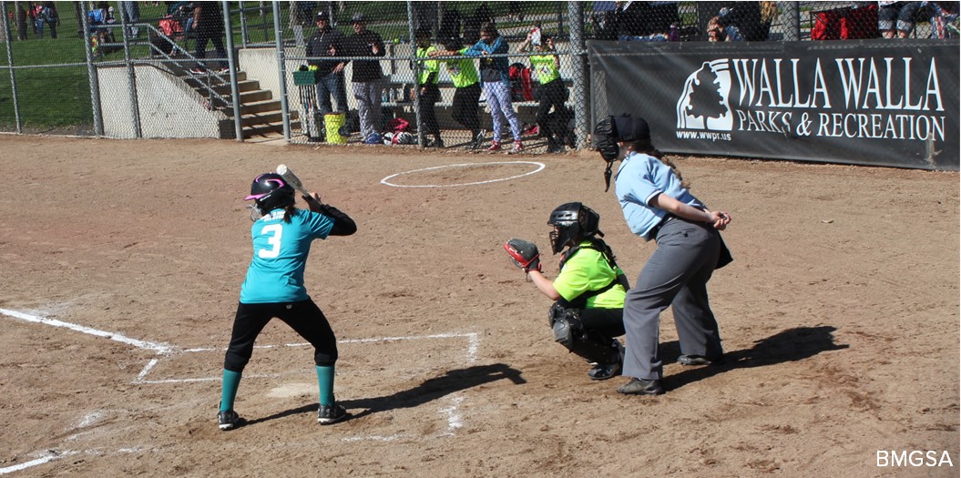 A softball batter and catcher wait for a pitch while an umpire looks on