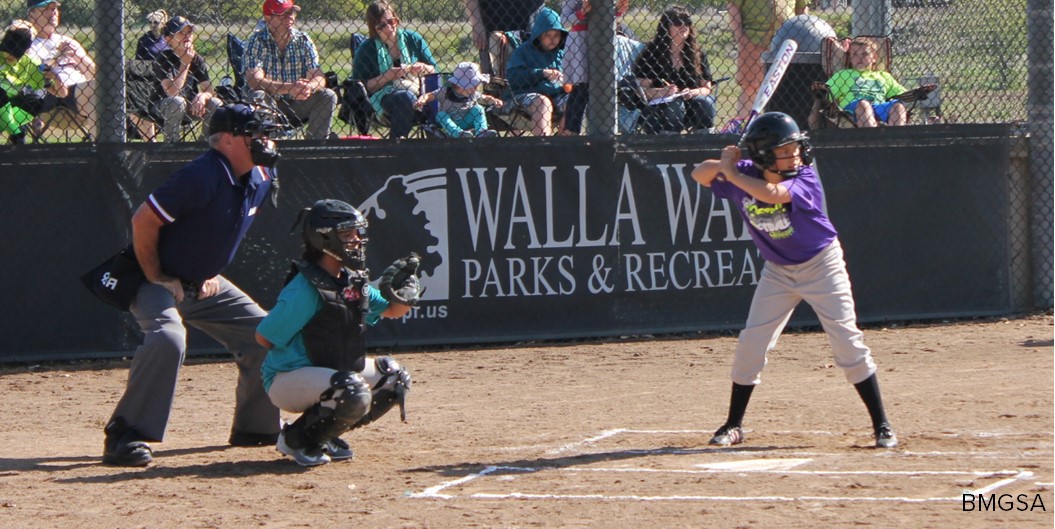 A softball batter and catcher wait for a pitch while an umpire looks on