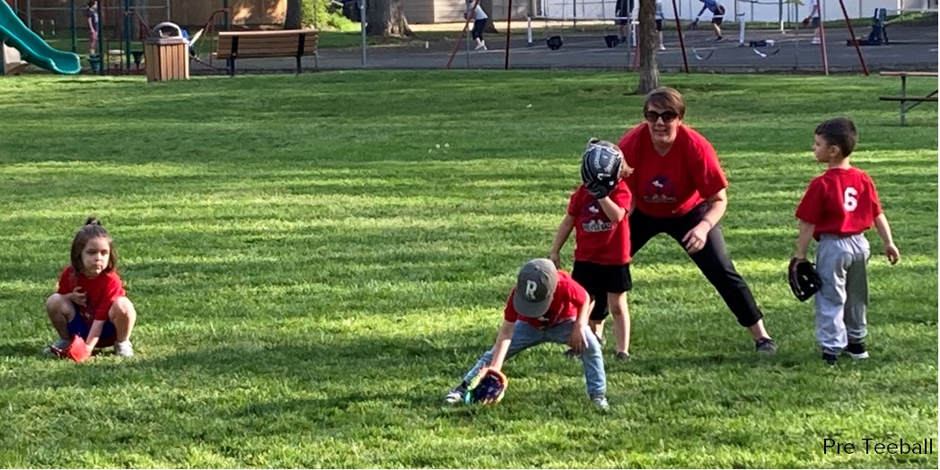 An adult coaches young children on how to field a baseball