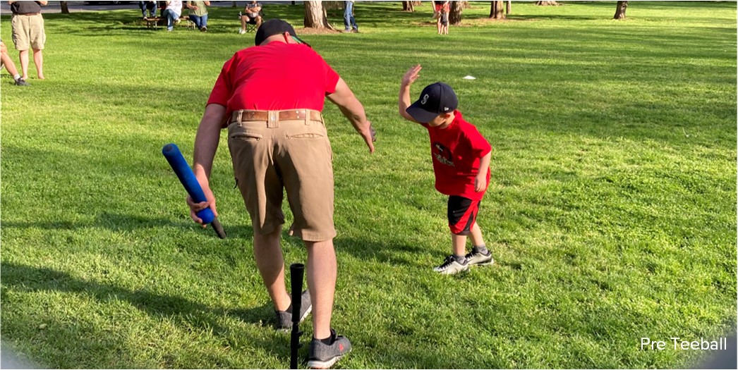 A young child gives a high-five to an adult coach holding a tee-ball bat