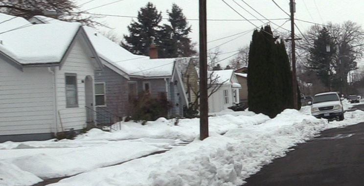 A berm of plowed snow along the curb of a residential street, blocking the driveway of a residence